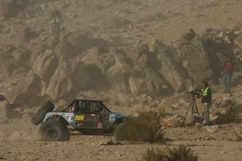 1992 Jeep Wrangler - An off-road buggy competes in a desert race, with spectators and a cameraman observing the action.