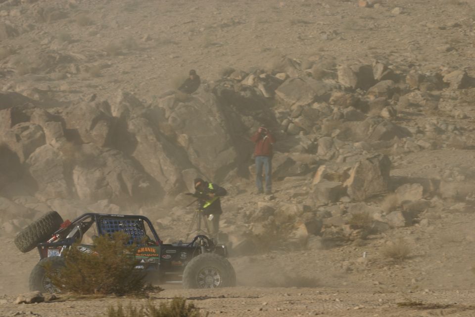 Off-road buggy with spare tire on back kicking up dust in a desert race
