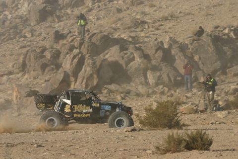 1992 Jeep Wrangler - A custom-built off-road buggy competes in a desert race, with spectators observing from the rocky terrain.