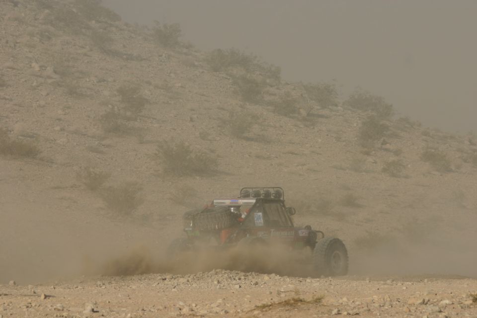 Off-road buggy kicking up dust on a dirt track, with a roll cage and spare tire visible