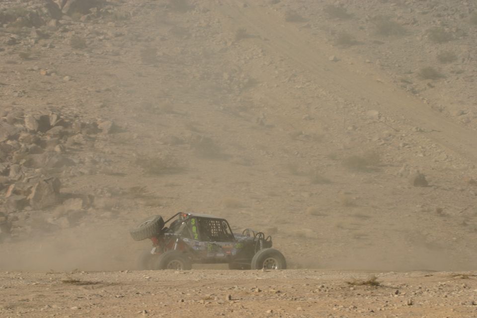Off-road buggy with spare tire mounted on rear, kicking up dust on a desert trail