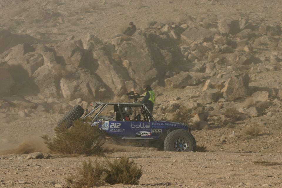Blue off-road buggy with number 212 on the side kicking up dust on a rocky desert terrain