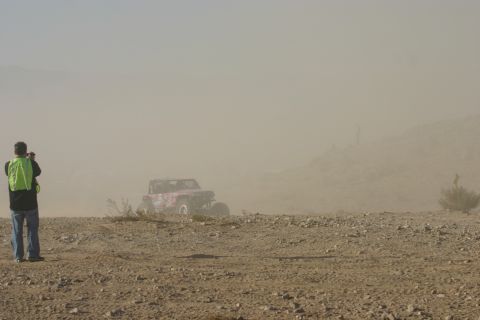1992 Jeep Wrangler - Off-road buggy races through a dusty desert landscape with a spectator observing.