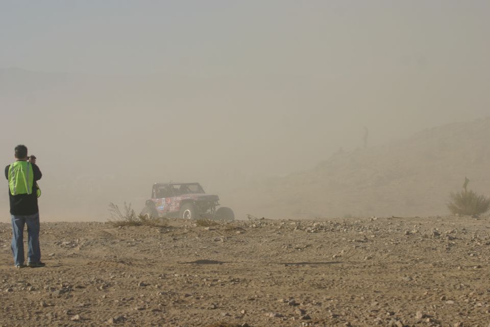 Off-road buggy kicking up dust on a dirt track, person with camera in foreground