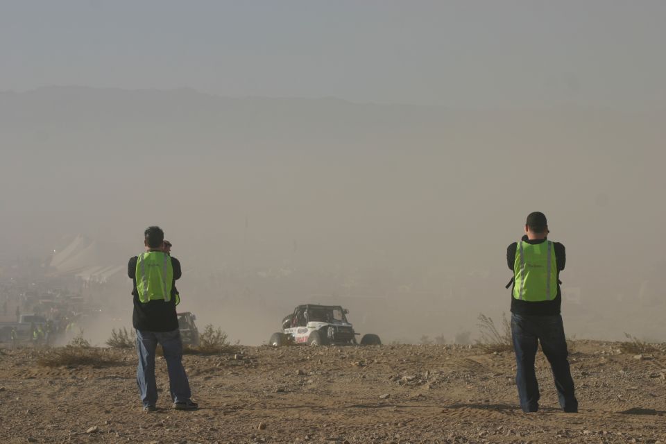 White and red off-road buggy with roll cage, seen in a dusty desert landscape