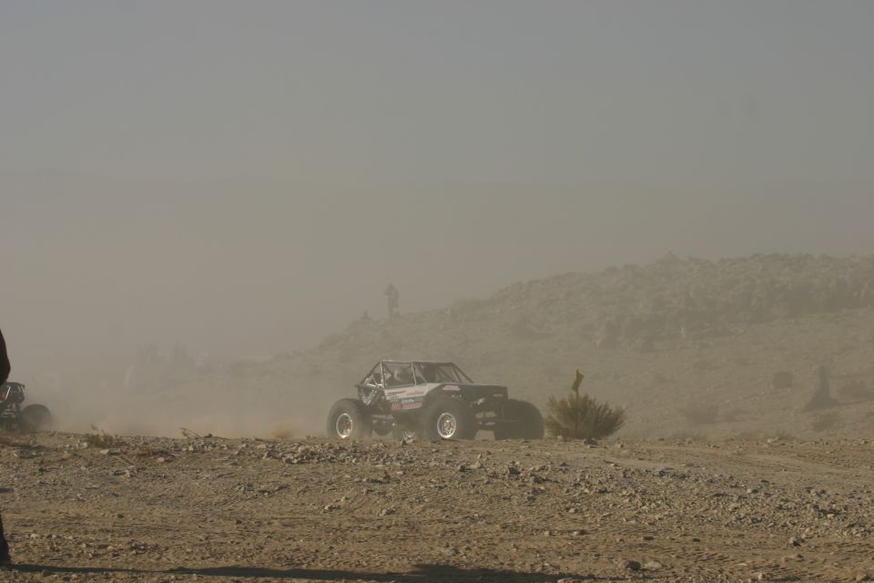 Off-road buggy kicking up dust on a rocky, barren hillside under a hazy sky