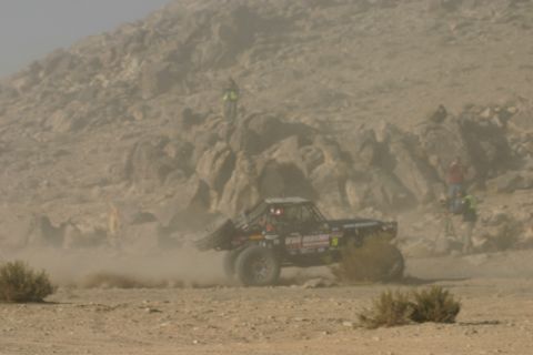 1992 Jeep Wrangler - An off-road buggy races through a dusty desert landscape, with spectators visible on a rocky hillside.