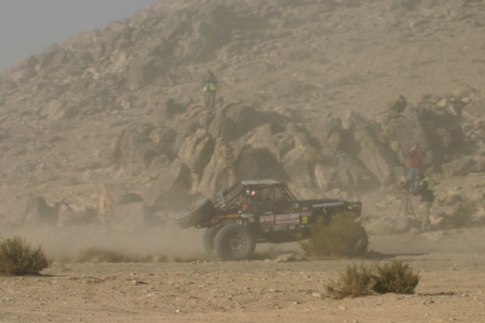 Off-road buggy in desert dust, side view. Some text visible on vehicle