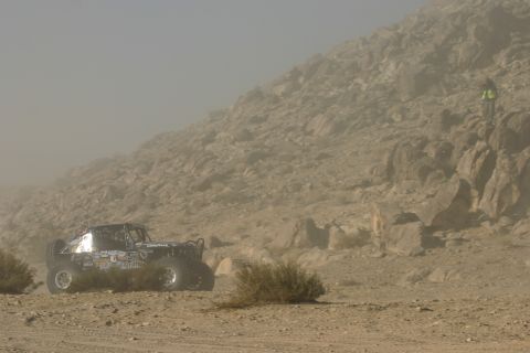 1992 Jeep Wrangler - Off-road buggy navigates dusty desert terrain with rocky hills in the background. A person observes from a higher vantage point.