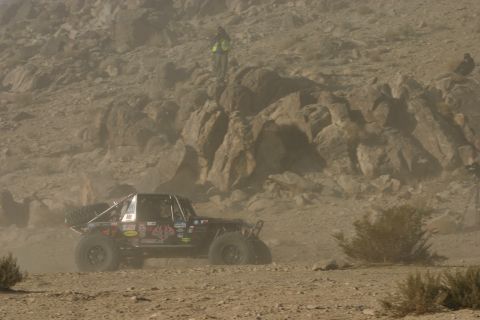 1992 Jeep Wrangler - A heavily modified off-road buggy navigates a dusty, rocky landscape, kicking up dust as it goes.