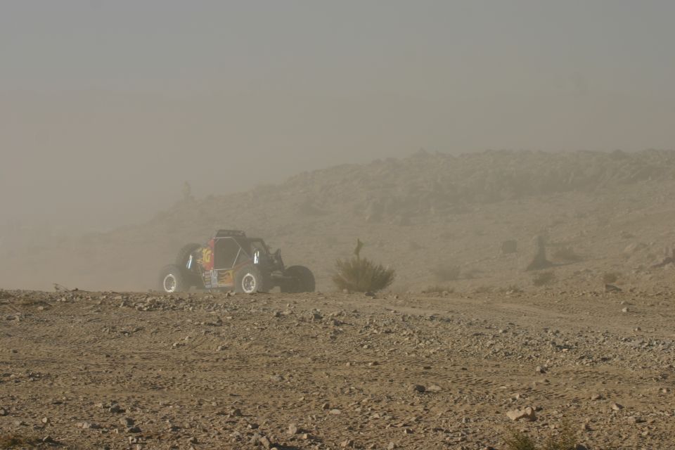 Off-road buggy with yellow and red decals driving on a dusty, rocky terrain