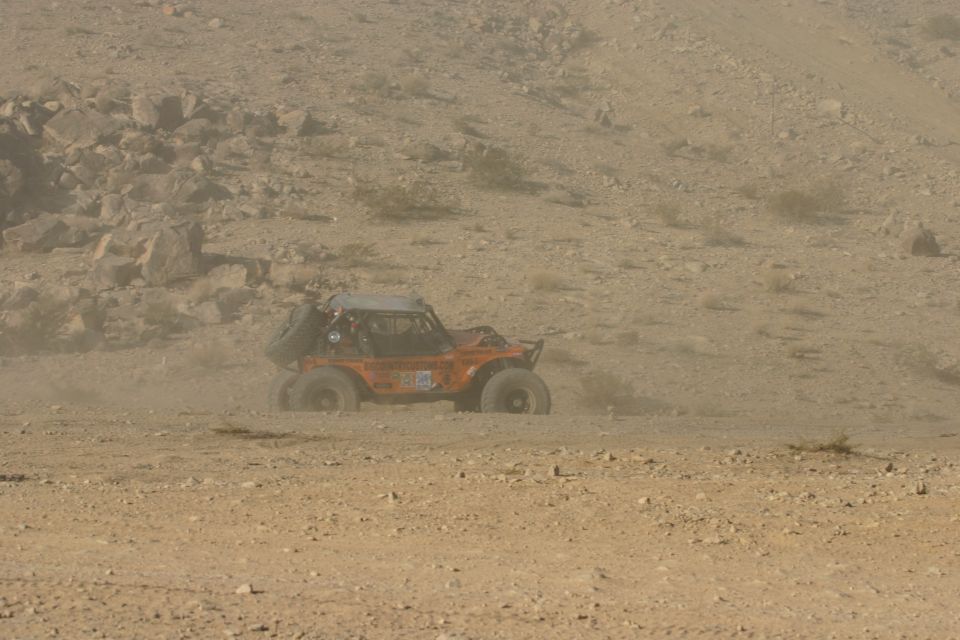 Orange off-road buggy with spare tire on back, kicking up dust