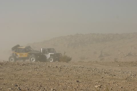 1992 Jeep Wrangler - Two off-road vehicles navigate a dusty desert environment, kicking up dust as they move.