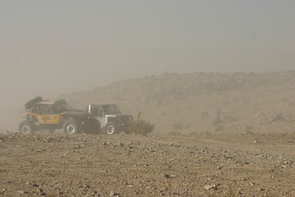 Two off-road vehicles, one yellow with number 4404, the other black, driving on a dusty desert terrain