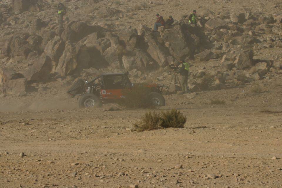Red off-road buggy with roll cage kicking up dust on a dirt track
