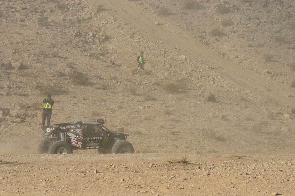 Black off-road buggy with Monster Energy sponsorship, kicking up dust on a desert course