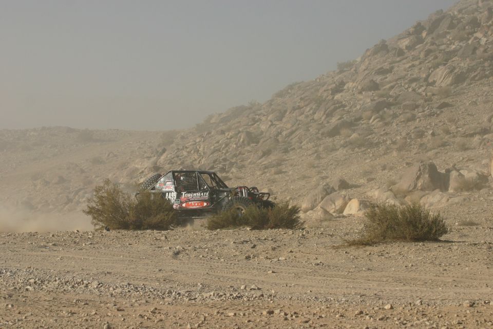 Black off-road buggy with red and white decals driving through a dusty desert landscape