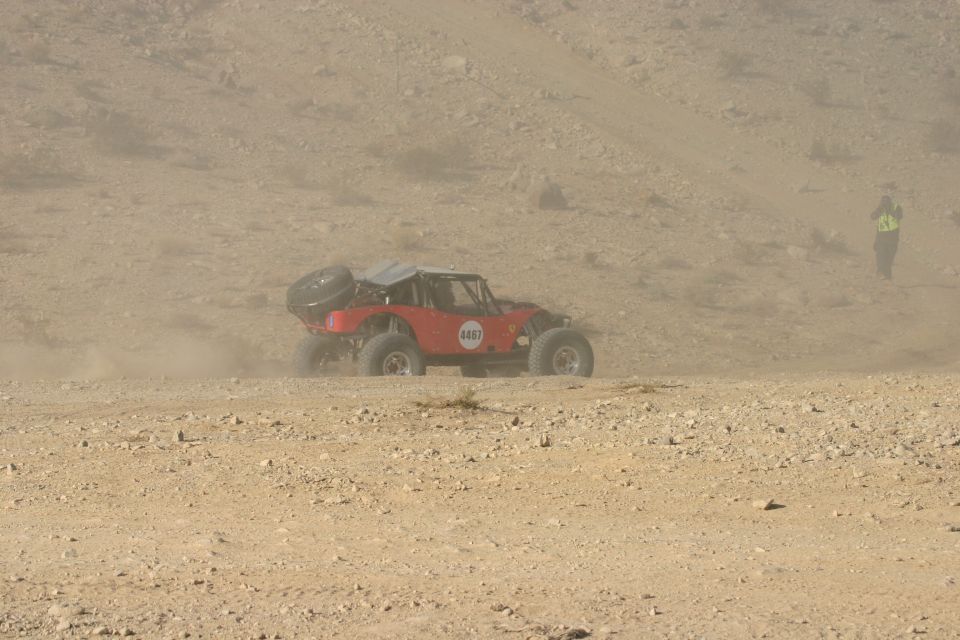 Red off-road buggy with a spare tire on the back, kicking up dust on a desert terrain