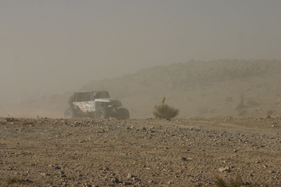 Modified Jeep driving on a dusty, rocky terrain. Decals visible on the side
