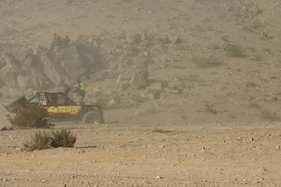 Off-road buggy with '4 WHEEL PARTS' on the side, kicking up dust in a desert race