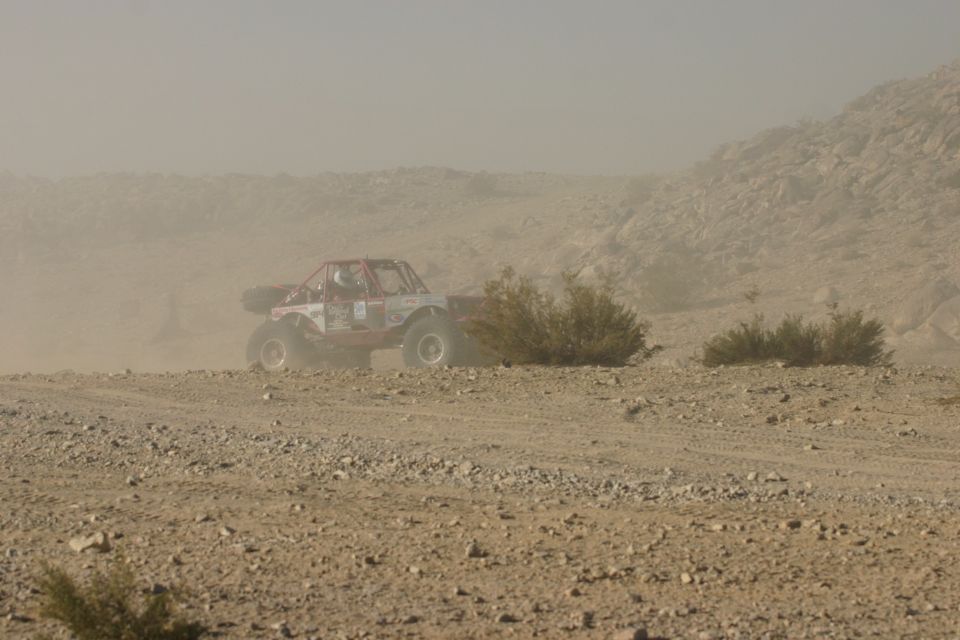 Red off-road buggy kicking up dust on a rocky desert terrain