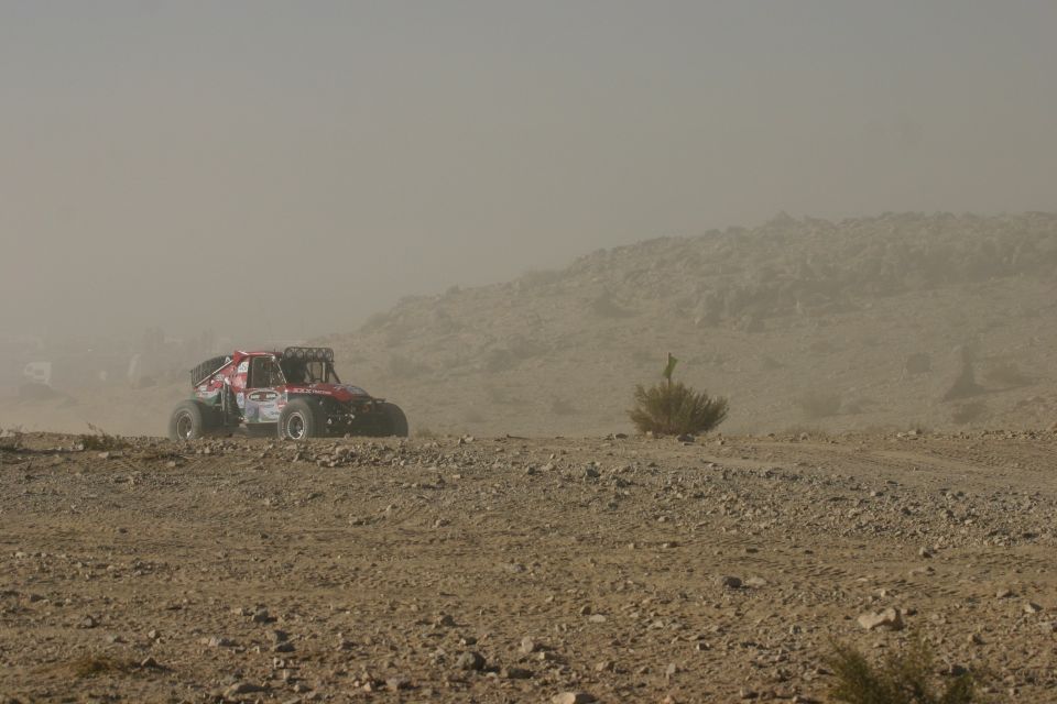 Red off-road buggy with large tires driving on a dusty, rocky terrain