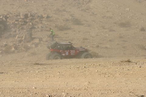 1992 Jeep Wrangler - A race buggy navigates a dusty desert terrain, with a person in a safety vest observing.