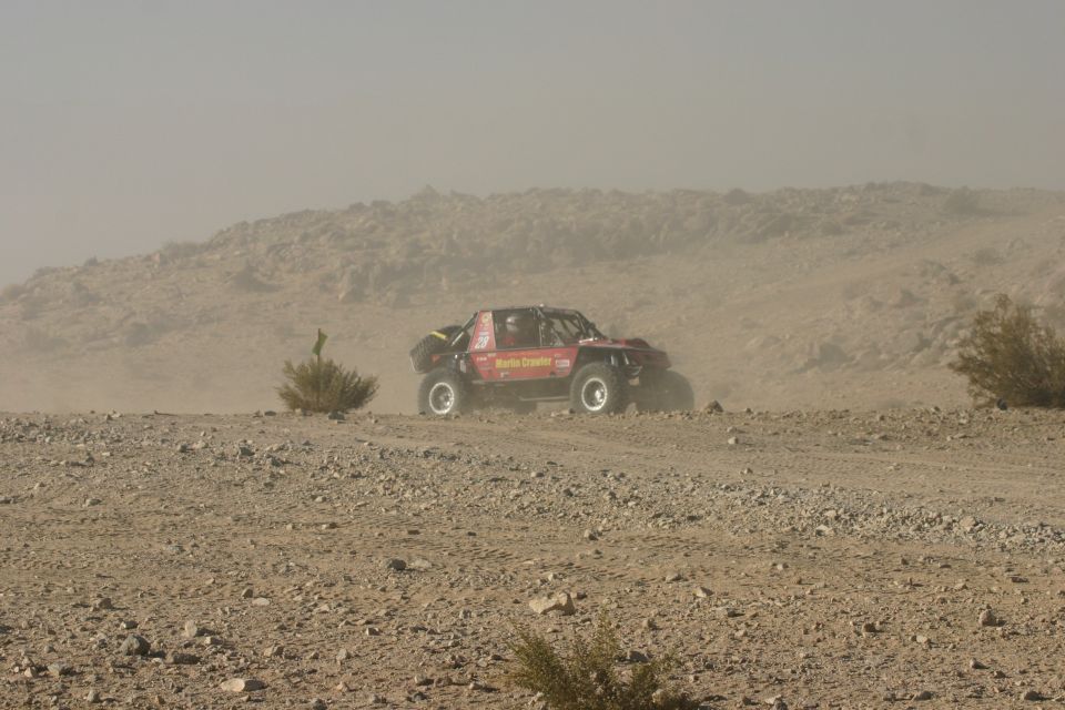Red off-road buggy with roll cage and "Monster Crawler.com" text on side, driving on dusty terrain