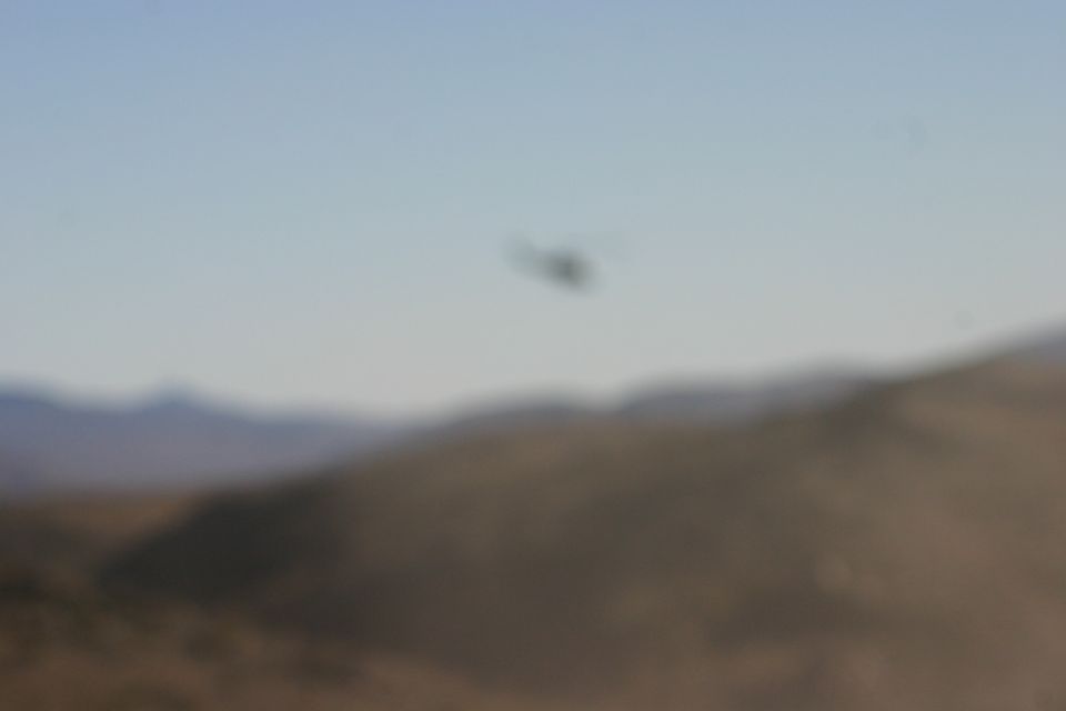 blurry helicopter flies over a desert landscape with mountains in the background