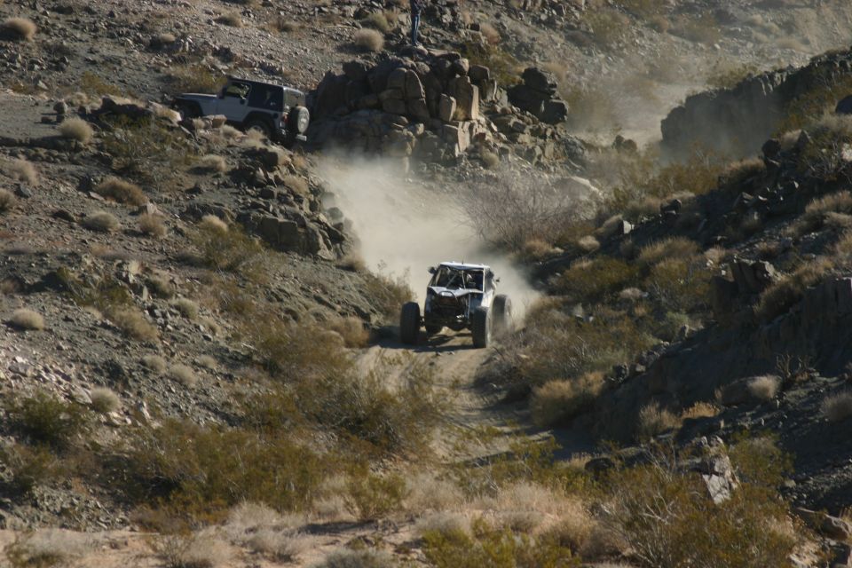 Off-road buggy driving on a dusty, rocky trail with another vehicle visible in the background