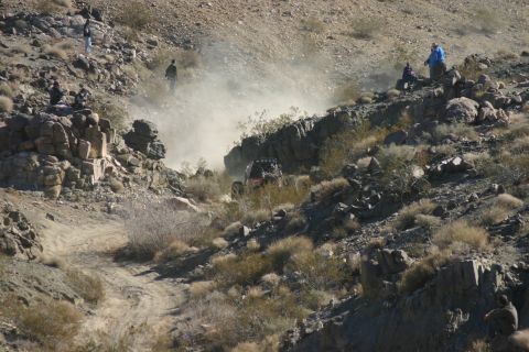 1992 Jeep Wrangler - An off-road buggy navigates a steep, dusty trail in a rocky desert landscape.