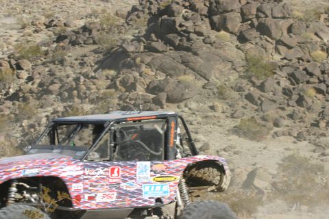 1992 Jeep Wrangler - A heavily modified off-road buggy navigates a rocky desert landscape during a race.