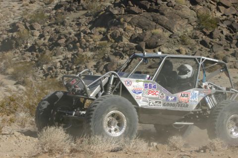 1992 Jeep Wrangler - A custom-built off-road buggy navigates a dusty, rocky terrain, numerous sponsor decals.