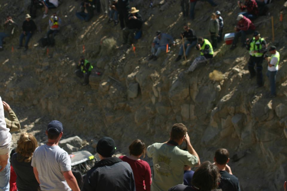 People gathered on a rocky slope, some watching an event below