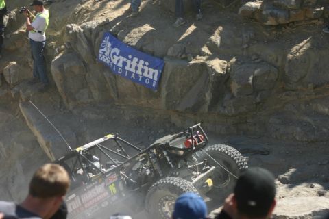 1992 Jeep Wrangler - An off-road buggy navigates a steep, rocky course, with spectators watching from the side.