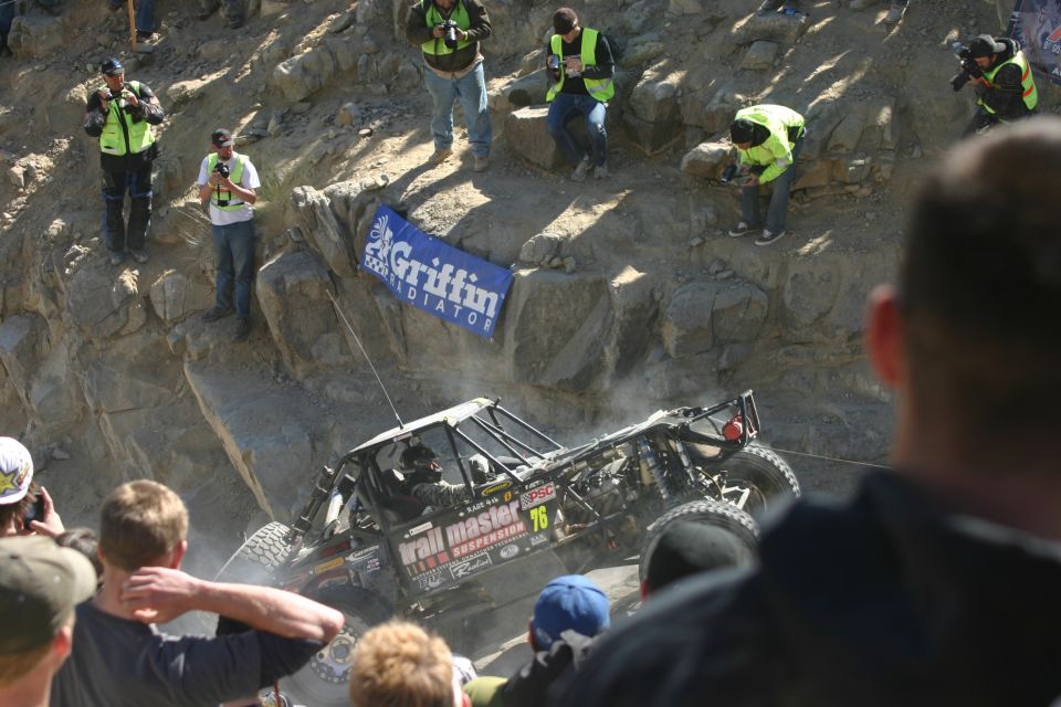 Off-road buggy with number 76 on side, climbing a steep, dusty rock face with spectators watching. Banner reads 'Griffin Radiator'