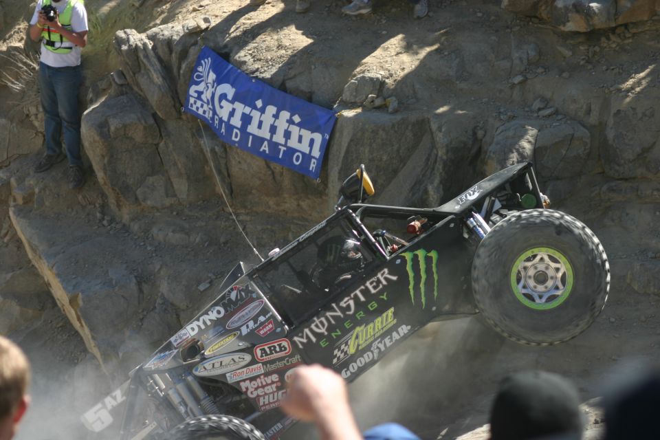 Black off-road buggy with Monster Energy logos climbing a rocky incline, front wheel in the air