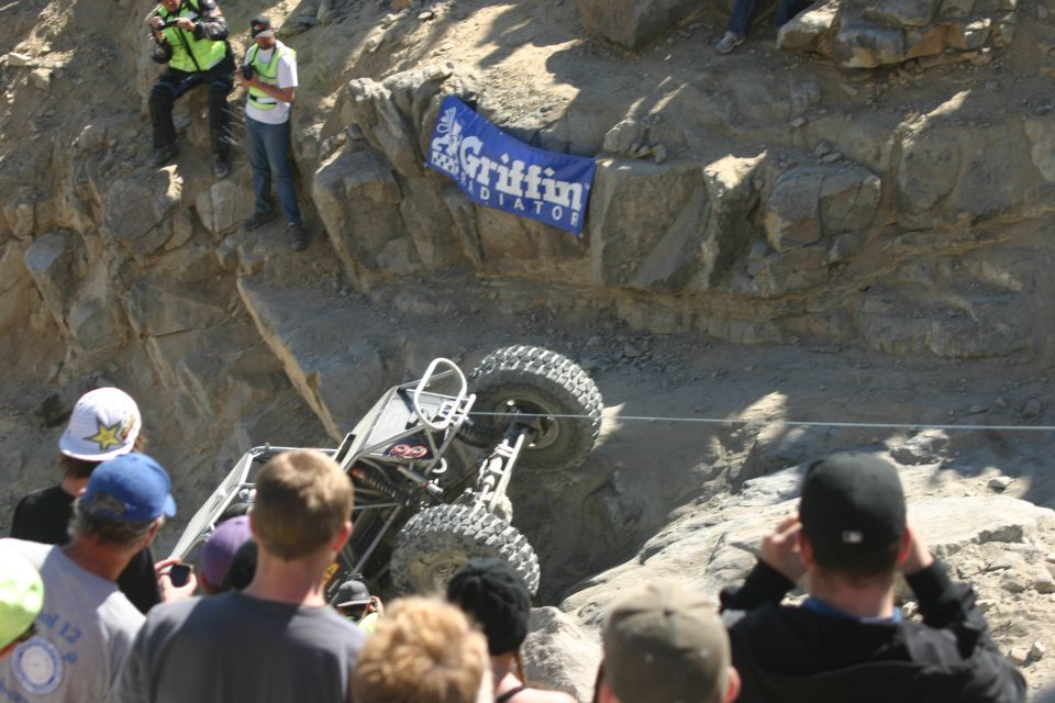 Off-road buggy tipped on its side on a rocky slope with spectators watching. A banner reads 'Griffin Radiator'