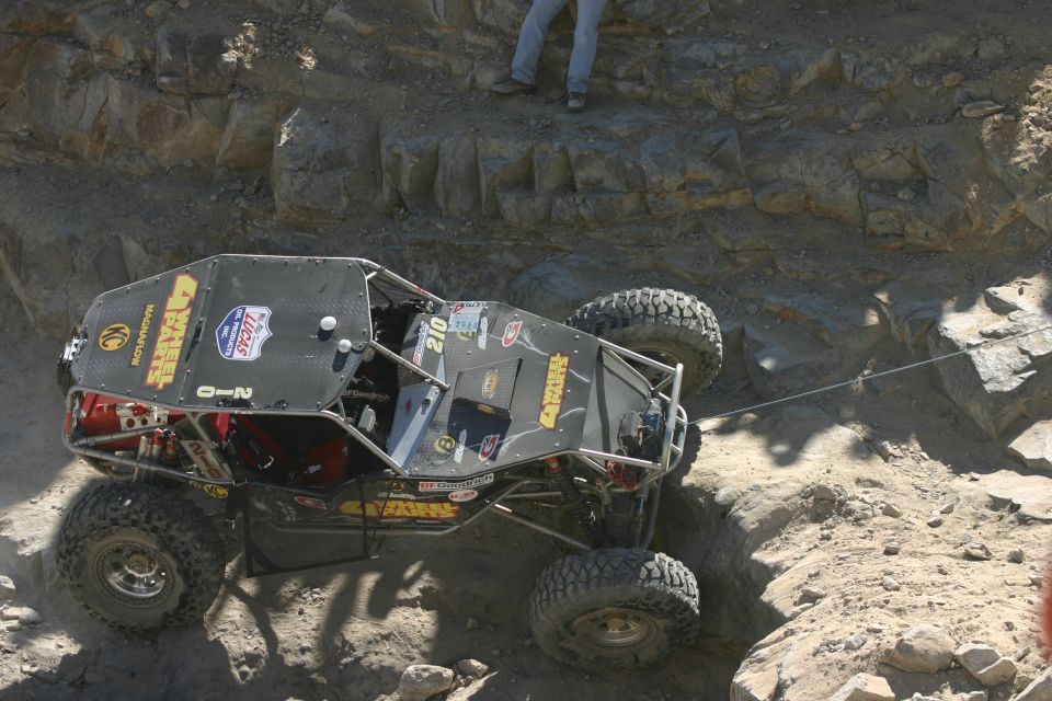 Custom off-road buggy with roll cage and large tires navigating a steep, rocky incline. Number 210 is visible on the side