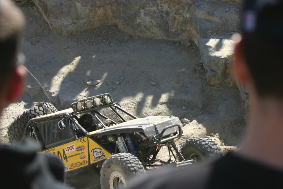 Yellow off-road vehicle with roll cage climbing rocky terrain. Visible text includes 'PSC' and a bulldog logo