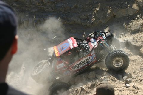 1992 Jeep Wrangler - A custom off-road buggy navigates a steep, rocky incline during a competition, generating significant dust.