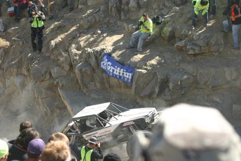1992 Jeep Wrangler - An off-road vehicle navigates a steep, rocky terrain during an event, with a crowd observing.