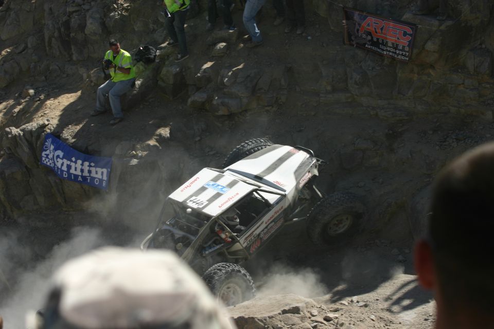 White off-road buggy with black stripes climbing a steep, dusty hill