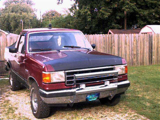 Maroon Ford pickup truck with black hood bra, parked outdoors