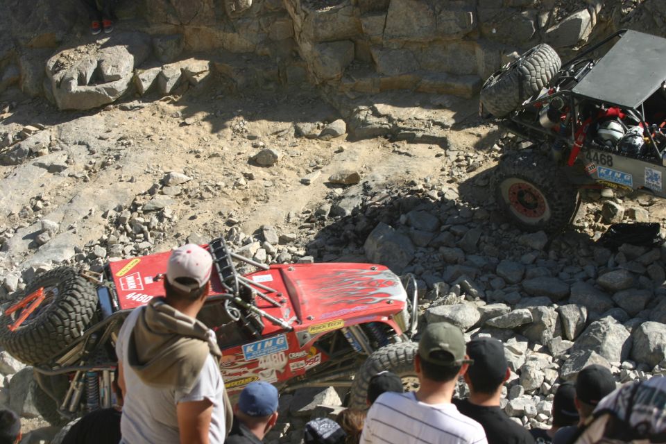 Red off-road Jeep Wrangler tipped on its side with flames graphic, and another off-road vehicle climbing rocks