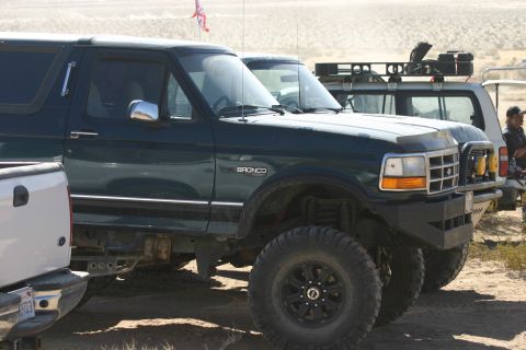 1992 Jeep Wrangler - A dark green Ford Bronco is parked in a desert landscape alongside other vehicles.