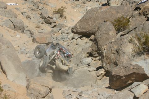 1992 Jeep Wrangler - A custom off-road vehicle attempts to ascend a challenging rocky terrain, kicking up dust.