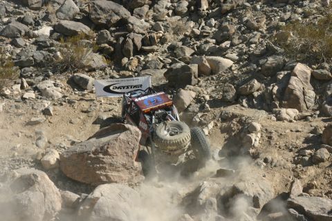 1992 Jeep Wrangler - Off-road buggy navigates a rocky terrain, kicking up dust. Daystar banner in background.