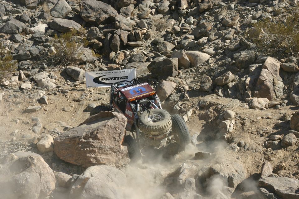 Off-road buggy with number 4485 on side climbing over large rocks, kicking up dust. Daystar banner visible