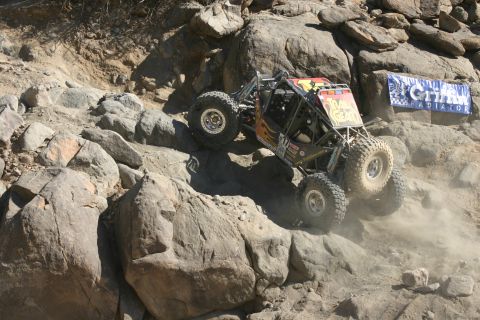 1992 Jeep Wrangler - Custom off-road buggy navigates a challenging rock course, dust billowing from its tires.